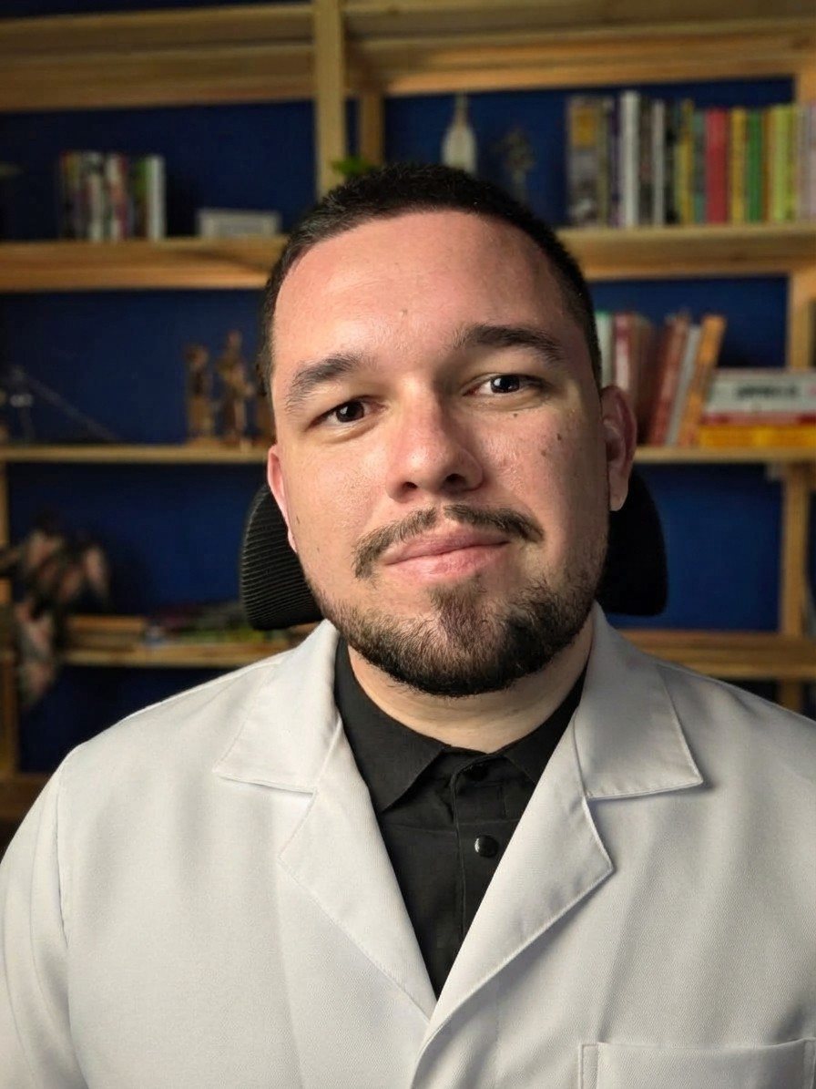 Allan Fernandes, nutricionista, de jaleco branco, sorrindo em frente a uma estante de livros